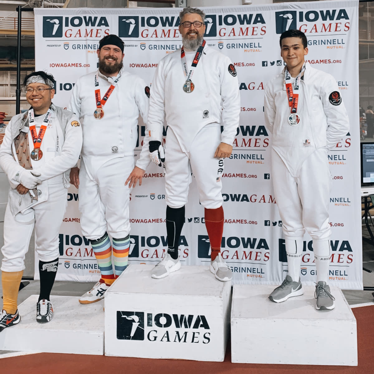 Eric Rhea atop the Iowa Games podium with the fencing gold medal, flanked by fellow medalists