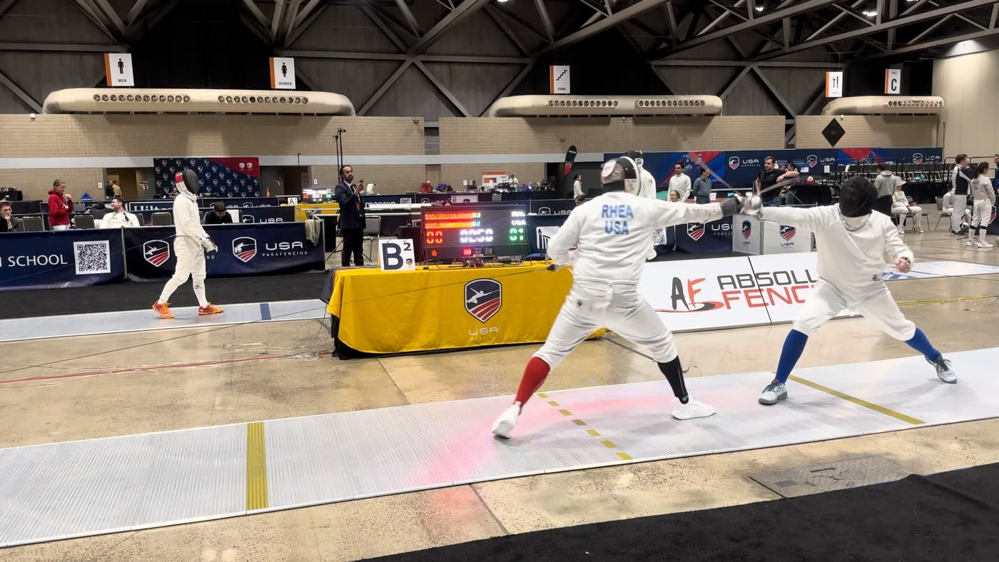 Eric Rhea lunging against an opponent on a national-event strip with scoring table behind